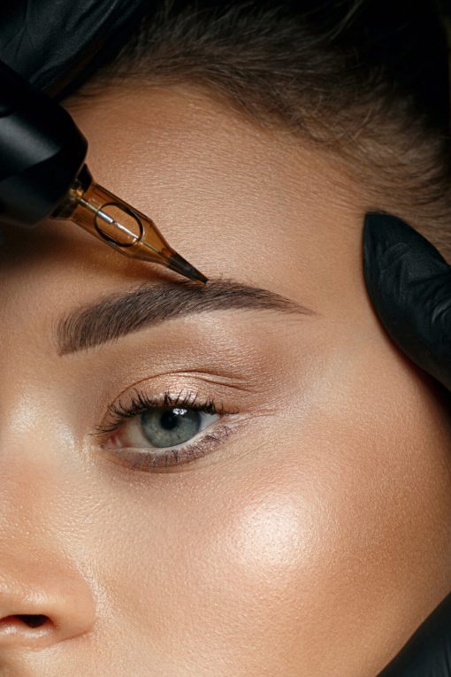 Beautician hand doing brow permanent makeup on an attractive female face