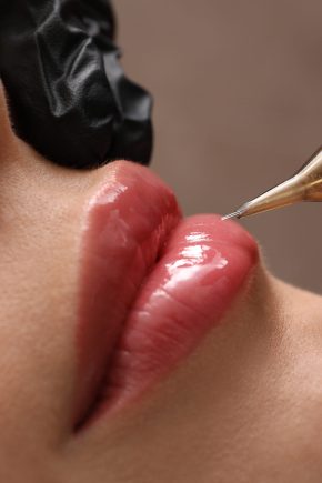 Young woman undergoing procedure of permanent lip makeup in tattoo salon, closeup